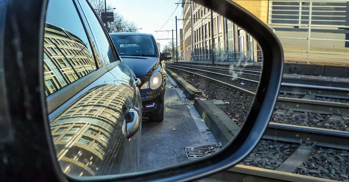 Autos und Bahnschienen im Rückspiegel eines Autos
