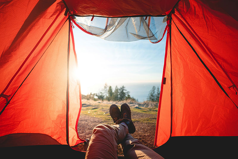 Blick aus einem Zelt auf Beine mit Boots und Panorama
